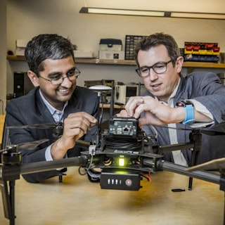 Two engineers smile as they work on a drone